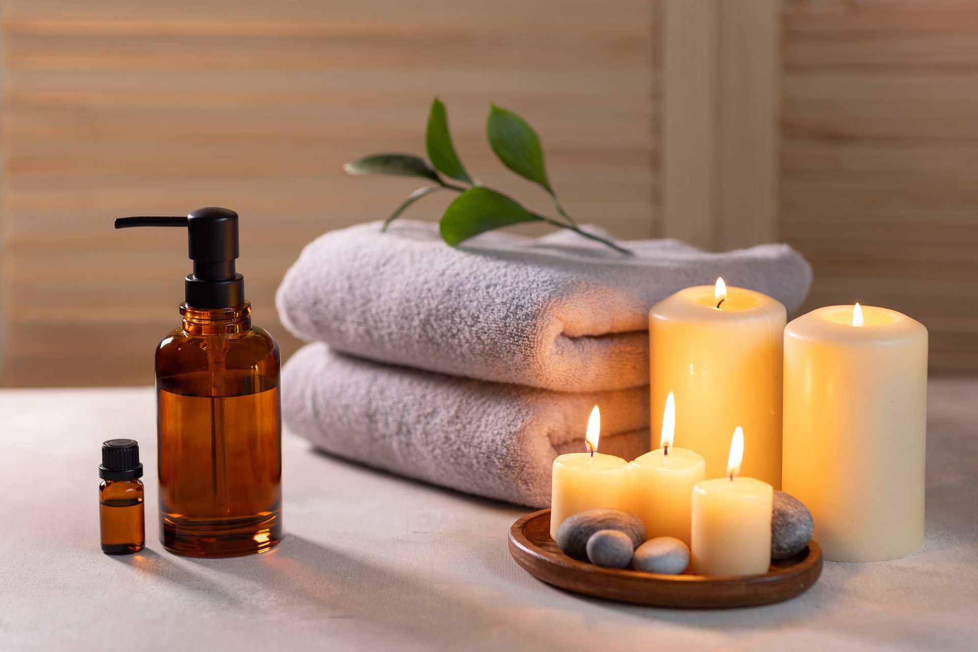 Beauty spa treatment items on white wooden table with candles stones essential oils and towels