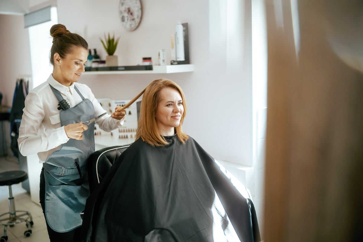middle aged woman hairdresser in modern hair studio with scissors and client cutting hair