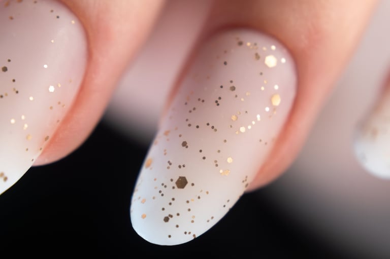A close-up of fingernails featuring a white polish base adorned with gold glitter